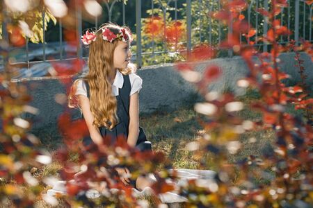 Little girl child sitting on lawn, girl blonde with long wavy hair with wreath of pink flowers.の写真素材