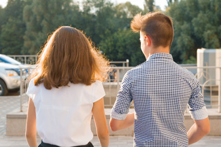 Youth boy and girl back view walking talking outdoor.