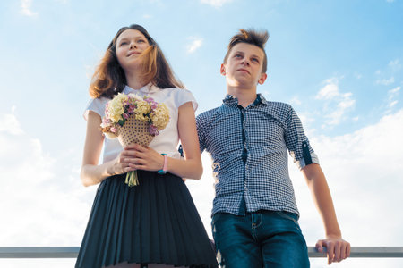 Happy couple of teens boy and girl 14, 15 years old. Young people smiling and talking, blue sky...