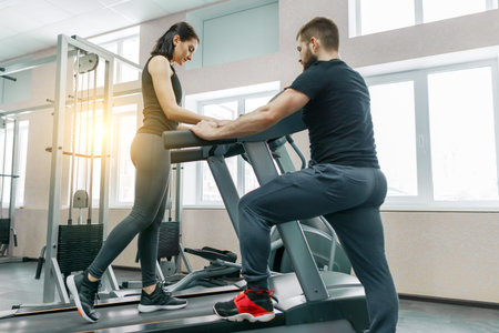 Young athletic women on treadmill, personal instructor coaching and helping client woman. Fitness,...