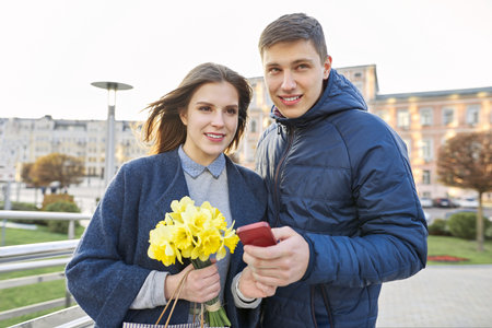 Outdoor portrait of beautiful romantic couple, young man and woman with bouquet of yellow flowers of...