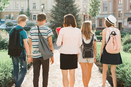 Outdoor portrait of school teacher and group of teenagers high school students. Children walking with teacher, view from the back.の写真素材