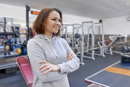 Portrait of smiling middle-aged confident woman with folded hands in the gym.