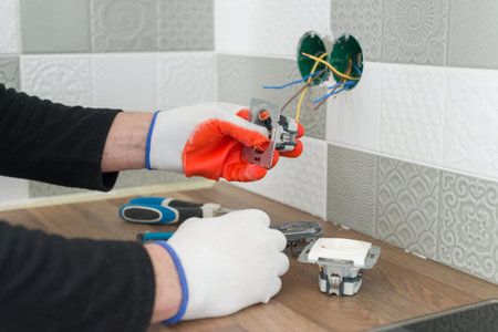 Renovation and construction in kitchen, close-up of electricians hand installing outlet on wall with...