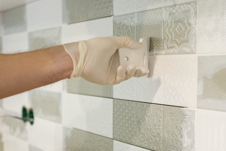 Closeup of tiler hand rubbing tile, Installing and grouting decorative finishes in environments with...
