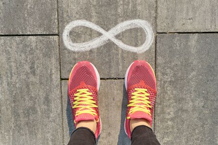Infinity sign on gray sidewalk with woman legs in sneakers, top view.の写真素材