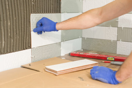 Closeup of tiler hand laying ceramic tile on wall in kitchen, renovation, repair, construction.