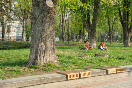 Kyiv UA, 23-04-2019. Young girls having a rest sitting on grass in city park, females with bicycles drinking water talking,のeditorial素材