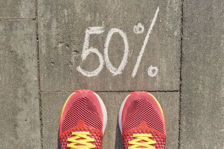 Text 50 percent written on gray pavement with woman legs in sneakers, view from above.の写真素材