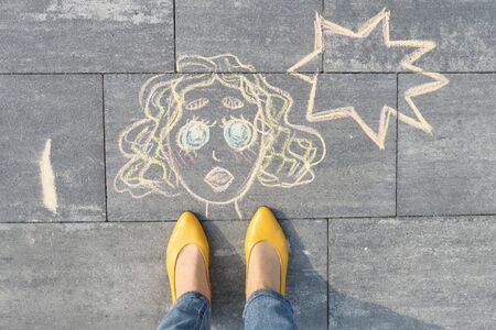 Abstract pop art woman face, picture written on gray sidewalk in crayons, with women legs in yellow shoes, top viewの写真素材