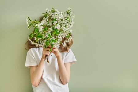 Girl child with spring white flowers blooming cherry branches, green wall background, copy space.の写真素材