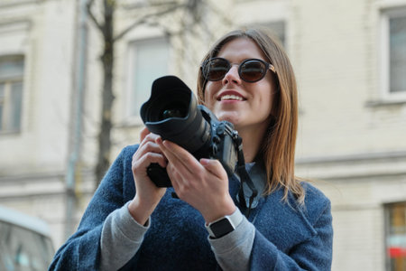Young beautiful girl with camera in the spring city, girl tourist taking photographs on city street.