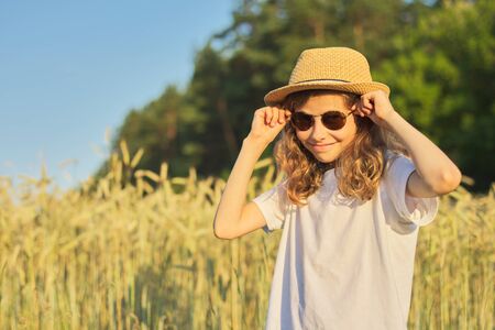 Girl child blonde in hat in wheat field, summer sunset, copy spaceの写真素材