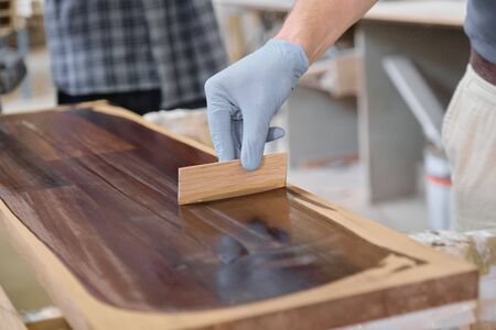 Closeup of workers hand covering wooden plank with finishing protective cover for wood, carpentry furniture woodworking productionの写真素材