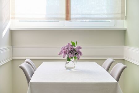 Living room dining area with 4 chairs near window, bouquet of lilac flowers on the table on white tablecloth. Home interior decorの写真素材