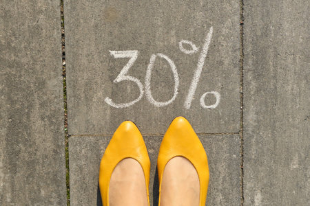 Text 30 percent written on gray pavement with woman legs, view from above.