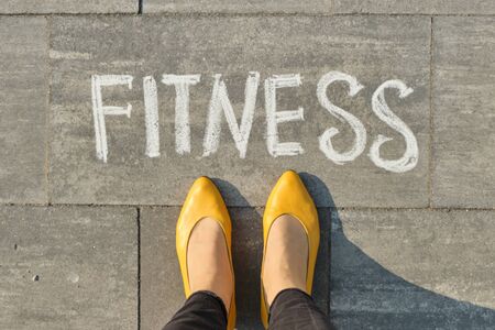Word fitness written on gray pavement with woman legs, view from above.の写真素材