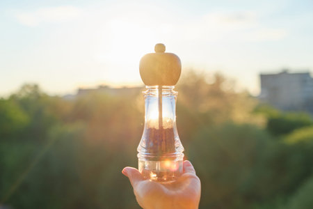 Black pepper peas in a mill in womans hand, background sunset, evening cityの写真素材