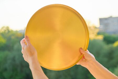 Round golden brass metal tray in womans hands, background sunset, evening cityの写真素材