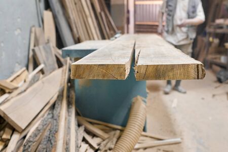 Male carpenter working on circular machine in workshop, worker cutting wooden plank on piece of furniture.の写真素材