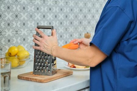 Woman hands rub carrot and apple on metal grater in kitchen. Homemade healthy food, cookingの写真素材