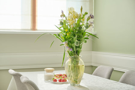 Home dining room interior, table with white tablecloth, spring summer bouquet of flowers in vase, tray with ripe strawberriesの写真素材
