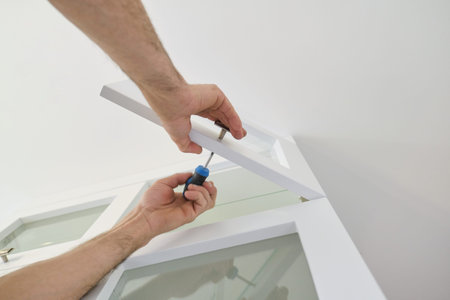 Working hands of male carpenter assembling furniture, close-up of installing door handles on door of...