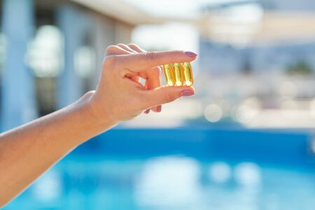 Sunny golden vitamin D oil capsules Omega-3 in woman hand, background sun blue water. Healthy lifestyle, nutritional supplements, dietの写真素材