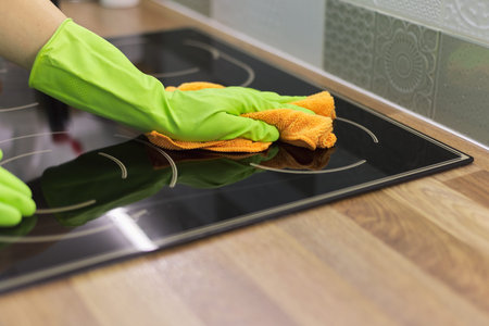 Woman hand in gloves cleaning kitchen electric ceramic hob, polishing glass with microfiber clothの写真素材