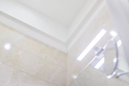 Bathroom interior, closeup detail. Part of the molding ceiling, LED light above the washbasin mirror, cosmetic makeup mirror, beige marble tiles on the wallの写真素材