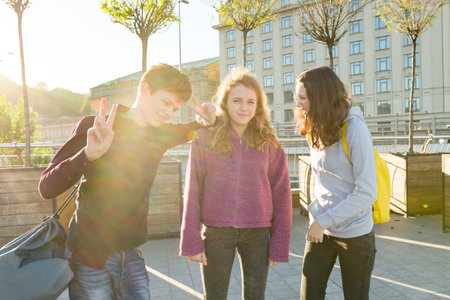 Friends teenagers students with school backpacks, having fun on the way from school. City...