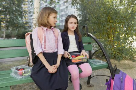 Autumn portrait of children with lunch boxes, school backpacks. Cheerful schoolchildren eat fruit, laughing, talking. Healthy food and healthy lifestyleの写真素材