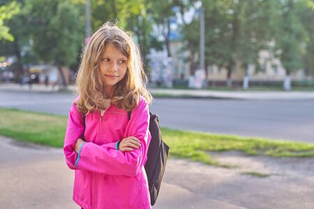 Portrait of school girl nine years old in jacket with backpack. Smiling child outdoors posing with folded arms, copy spaceの写真素材