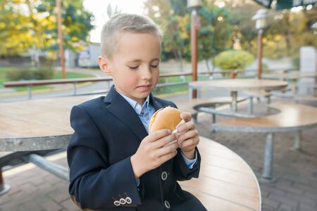Boy primary school student eats burger, sandwich at an outdoor cafeの写真素材