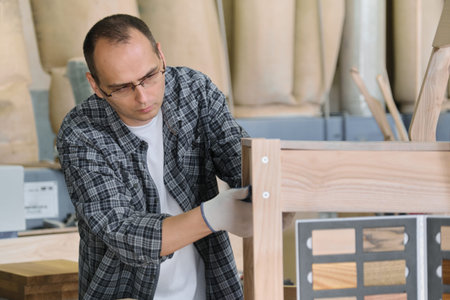 Furniture production, portrait male carpenter in wood workshop making wooden chair.