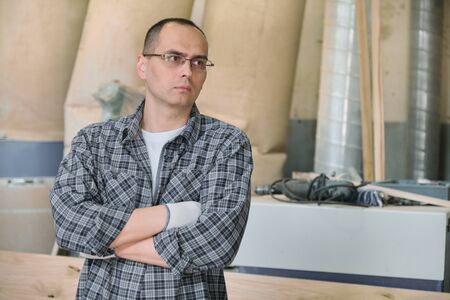 Portrait of male worker in industrial production. Confident man in glasses gloves in casual shirt with crossed arms, copy spaceの写真素材
