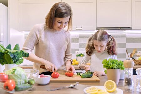 Mother and daughter cooking together in kitchen vegetable salad, parent and child are talking smilingの写真素材