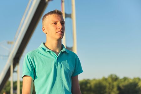 Outdoor portrait of young blond male, serious confident teenager, background blue sky, sunny summer day, copy spaceの写真素材