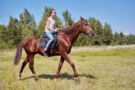 Teenager girl riding a brown horse, horseback riding for people in the park.の写真素材