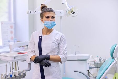 Portrait of confident female dentist doctor in white coat with mask near dental chair in dental clinic officeの写真素材