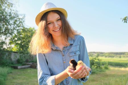 Outdoor portrait of beautiful smiling teenage girl on farm with two newborn chicks in handの写真素材
