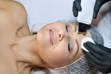 Cosmetology, mature woman receiving face cleaning with an ultrasonic device spatula facial cleanser...