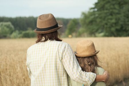Mother hugging her little daughter back view, yellow ripe wheat field nature background, sunset golden hourの写真素材