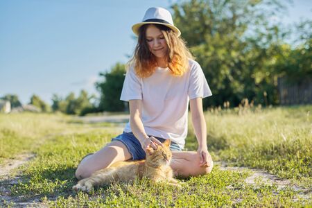 Teenager girl in hat on nature playing with red cat, rustic style, girl and pet on country road on sunny summer dayの写真素材