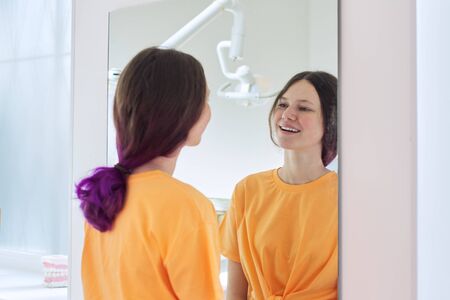 Beautiful teenager girl looking at white healthy teeth in mirror in dentist office. Medicine, dentistry and healthcare conceptの写真素材