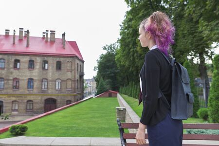 Back to school, college. Outdoor teenager girl student with trending hairstyle with backpack in school uniform. Girl looking at school building, copy spaceの写真素材