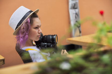Teenager girl with camera sitting in an city outdoor cafe, holding camera in her hands, female...