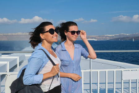 Two traveling women, mother and teenage daughter in luxury travel Mediterranean. Smiling females on open deck of cruise liner, background sea sky, Santorini islandの写真素材