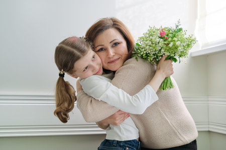 Mother hugging her little daughter with bouquet of beautiful spring flowers, congratulations and childs gift to parent on mothers dayの写真素材