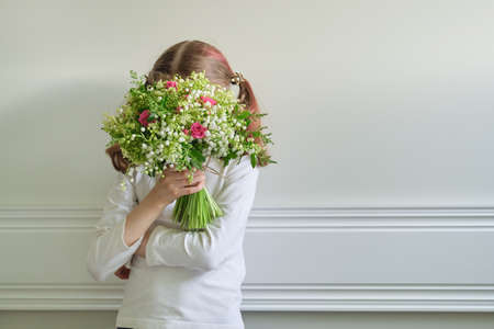 Child girl with bouquet of beautiful spring flowers, face covered with bouquet, gift on Mothers Day, on March 8. Copy spaceの写真素材